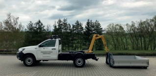 Bílá dodávka s hydraulickou rukou a kontejnerem na odpady.