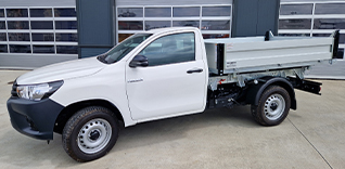 Bílá Toyota Hilux s hydraulickou sklápěcí korbou.