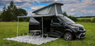 Černá dodávka s markýzou a střešním stanem na louce.