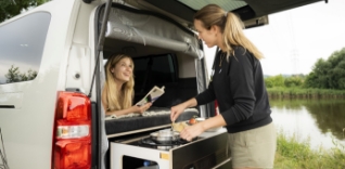 Dvě ženy si vaří v přestavěné dodávce u jezera.