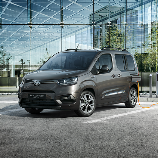 Elektrické rodinné MPV Toyota Proace City Verso na parkovišti před moderní budovou.