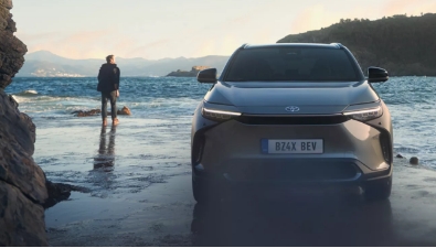 Stříbrné elektrické SUV na pláži s mužem v pozadí.